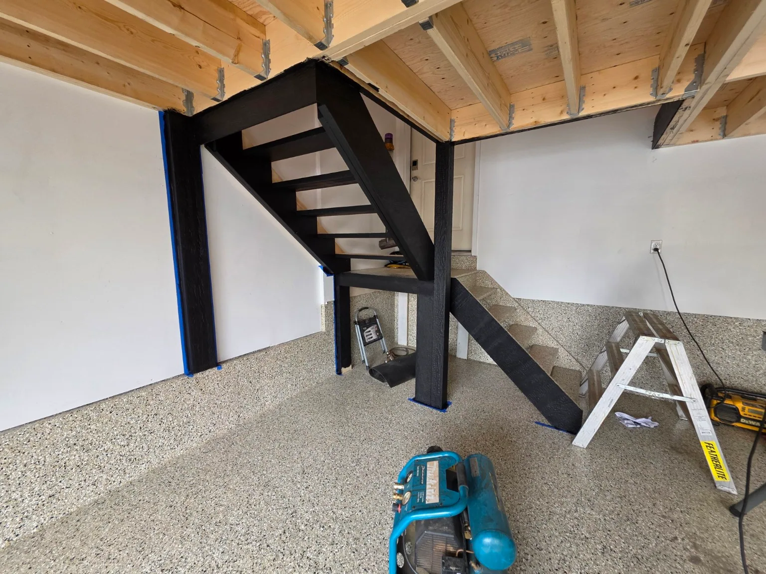 Garage mezzanine during construction, showing timber framing, black posts and unfinished stair access