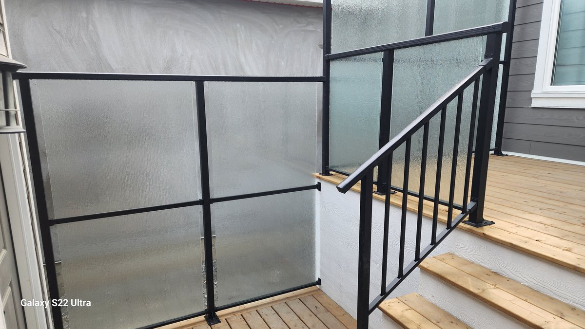 Textured glass privacy panels in black frames beside picket stair railing